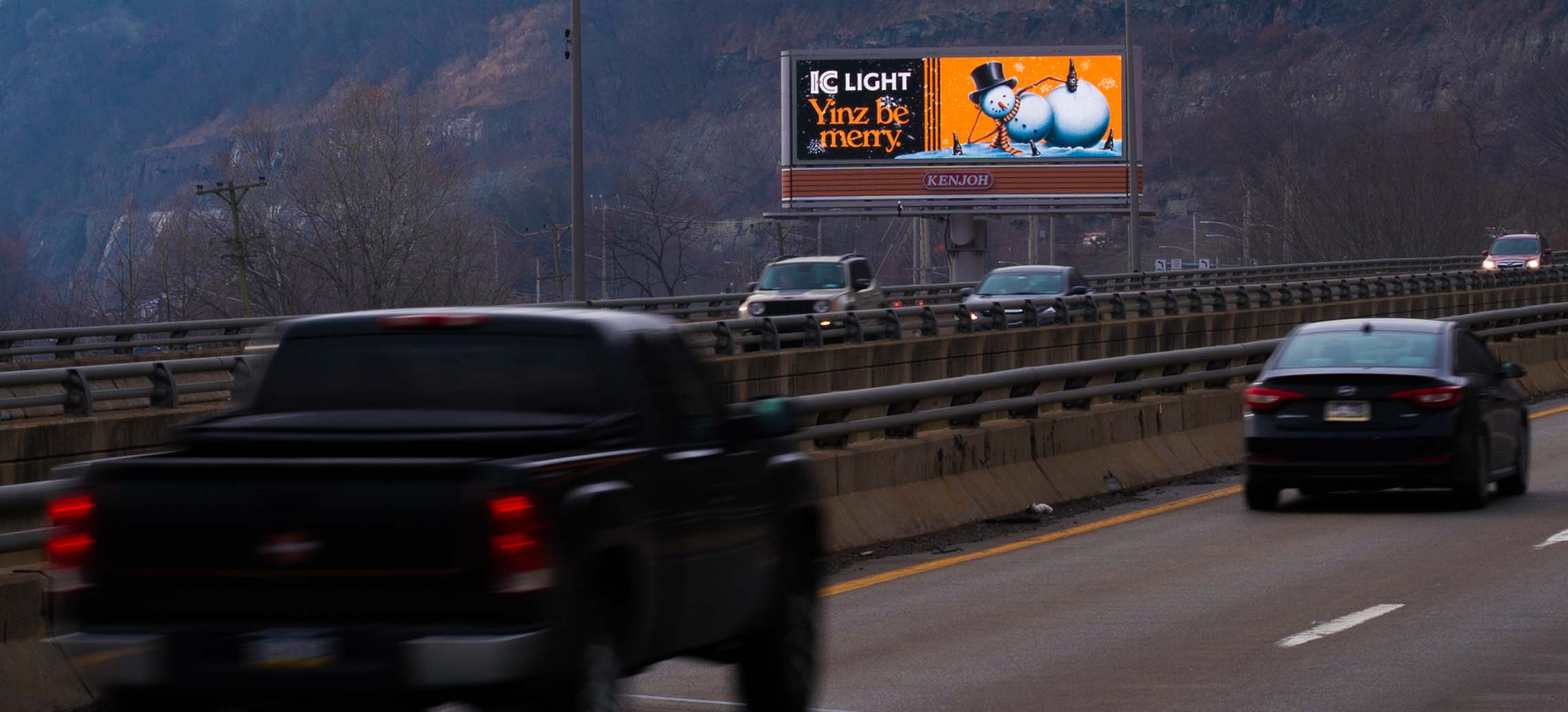 Digital billboard advertising a holiday beer campaign above a busy highway