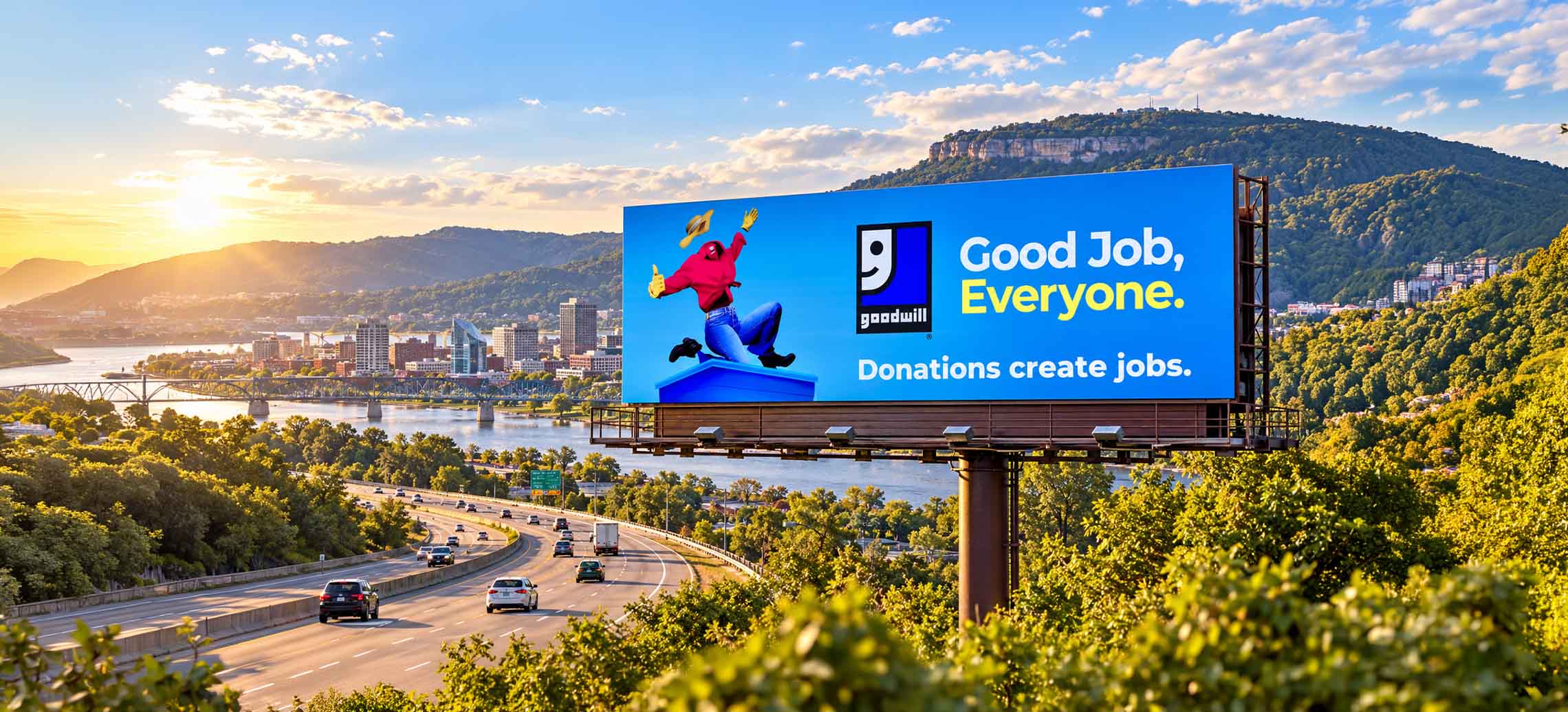 Goodwill billboard above a highway overlooking a river valley at sunset
