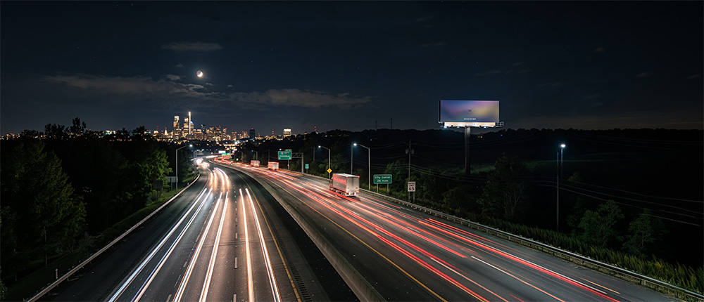Nighttime highway with light trails leading toward a digital billboard