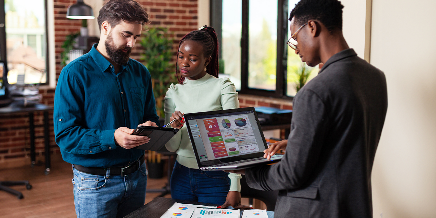 Group of coworkers discussing charts and colorful marketing visuals in an office.
