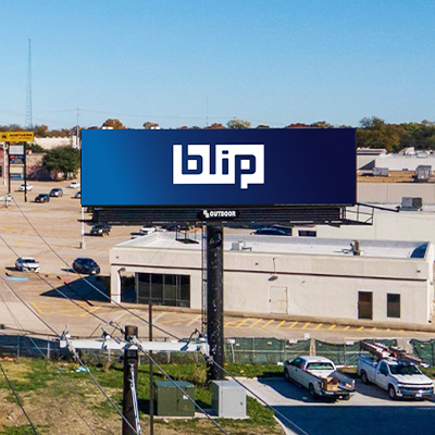 Blue Blip billboard above commercial area with parked cars and low-rise buildings.