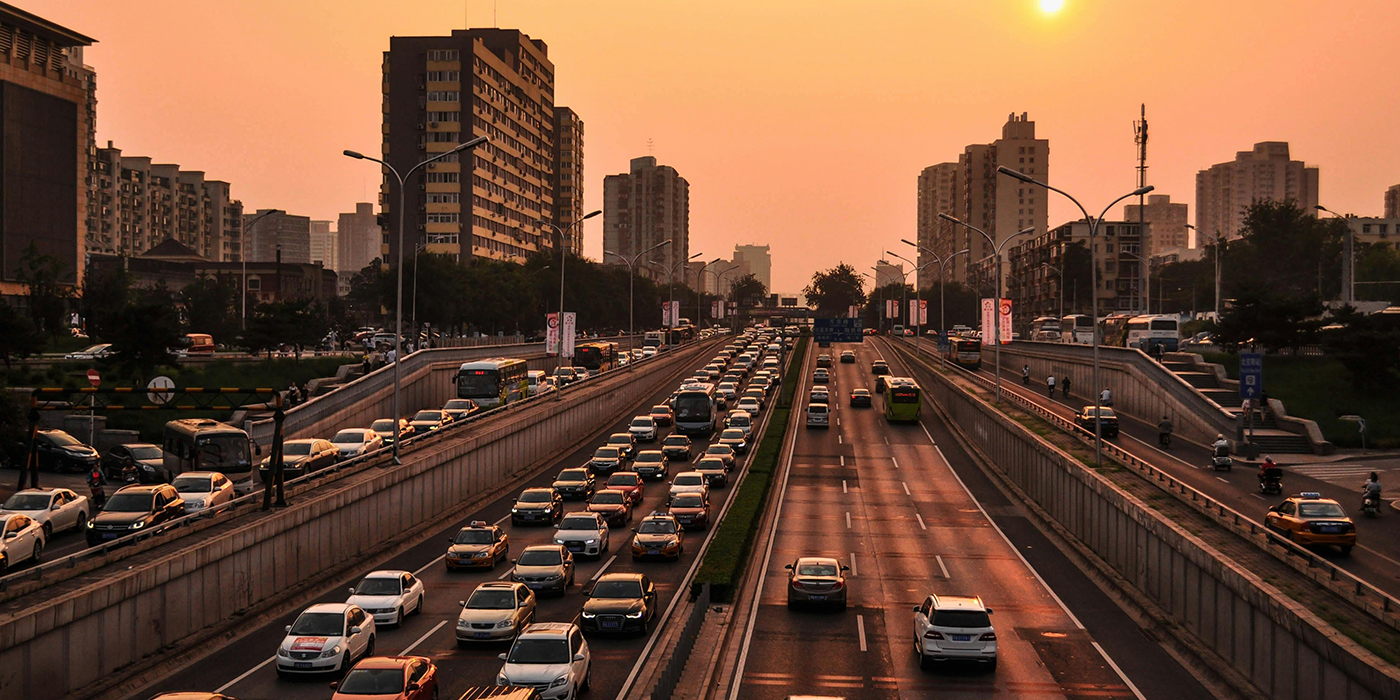 Dense traffic on a city highway at sunset with tall buildings in background.