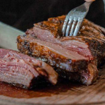 Sliced steak with fork on cutting board