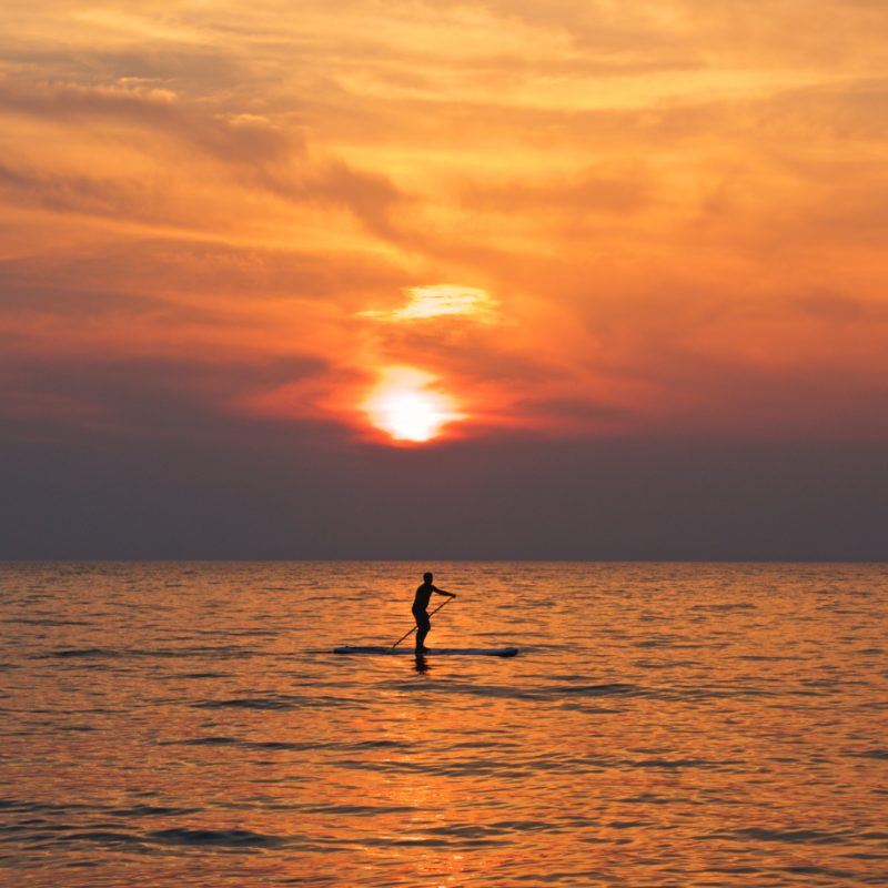 Person on calm water at orange sunset