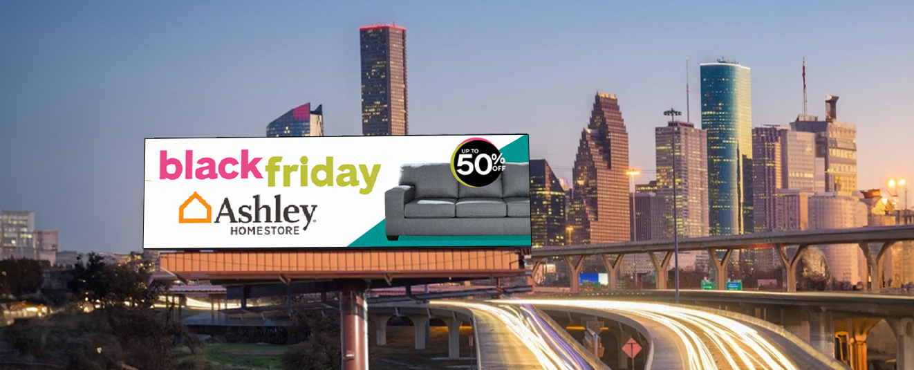 Large digital billboard for Ashley HomeStore Black Friday sale with “up to 50% off” sofa promotion on a highway overpass at dusk.
