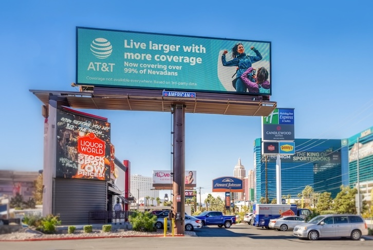 AT&T roadside billboard saying “Live larger with more coverage” above busy street.