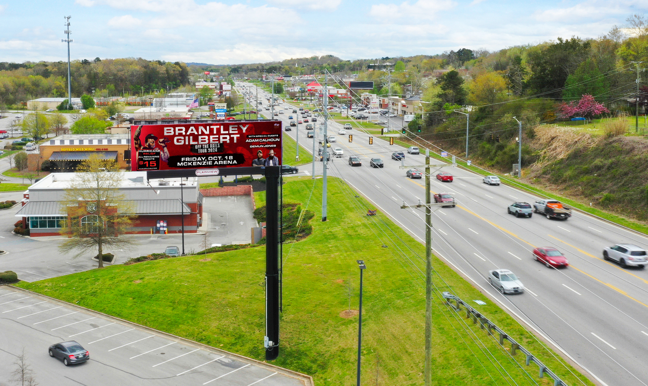 Red concert billboard advertising Brantley Gilbert Off The Rails Tour with special guests and ticket details, overlooking a suburban road.