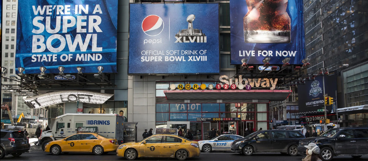 Times Square scene with huge Pepsi Super Bowl ads and yellow taxis in front of a Subway entrance